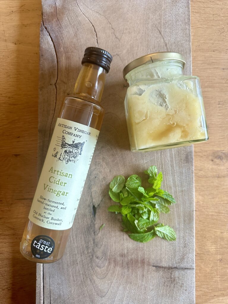 A jar of wildflower honey, mint leaves and cider vinegar with cutting board